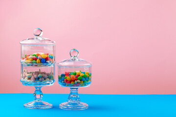 Glass containers with candies against pink background