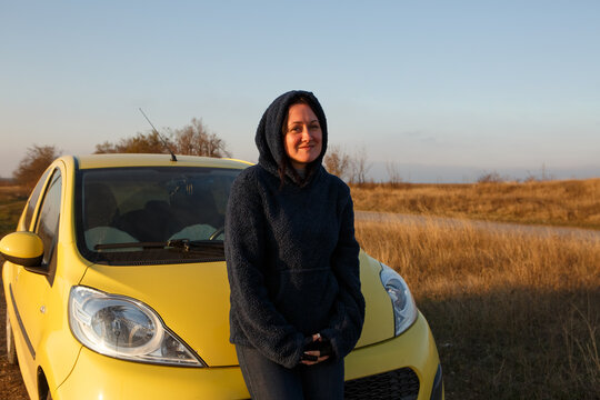 Woman Standing Outdoors In A Yellow Car On A Background Of Blue Sky