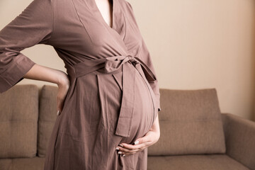 Pregnant woman hold back pain on sofa at thr home. Maternity healthcare concept support products