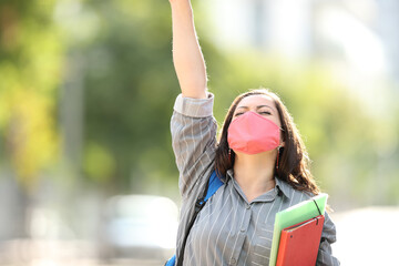 Naklejka premium Excited student wearing mask raising arm in the street