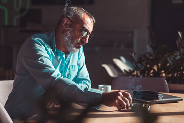 Middle aged bearded man drinking first morning coffee and smoking