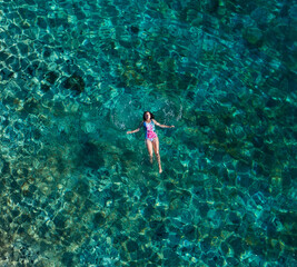 Young female floating on the back and relaxing on the warm turquoise Adriatic sea waves with rocky...