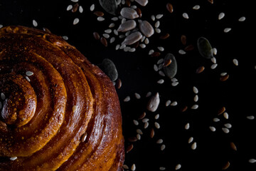 A bread roll with seeds on black background. Top view. Flatlay