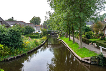 A canal flowing between buildings in a famous village in the Netherlands, visible trees and flowers in the gardens.