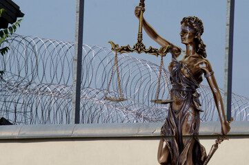 Lady Justice in front of barbed wires and prison walls
