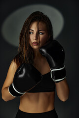 portrait of gorgeous sporty woman in boxing gloves on black studio background
