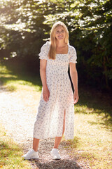 Fototapeta na wymiar Full Length Portrait Of Smiling Woman Wearing Summer Dress Walking Along Countryside Path
