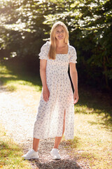 Full Length Portrait Of Smiling Woman Wearing Summer Dress Walking Along Countryside Path