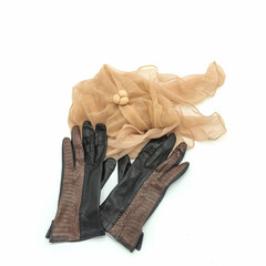 Autumn accessories. A pair of brown ladies' gloves made of genuine leather, decorated with an embossing imitating the skin of a snake. Light beige translucent scarf. Isolated over white background.