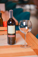 Wine glass and bottle of red wine on a wooden table over blurred background. Restaurant service, eating out concept.
