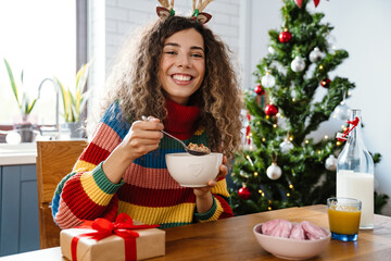 Joyful charming woman in toy deer horns smiling while having breakfast