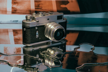 Old retro vintage film camera lying on the table with reflection on the mirror glass surface 