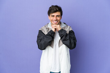 Young cool man keeps hands under chin, is looking happily aside.