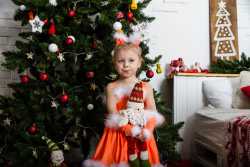 Christmas, New Year tree.  A little girl in a fluffy, red dress and ears on her head is standing under the Christmas tree.