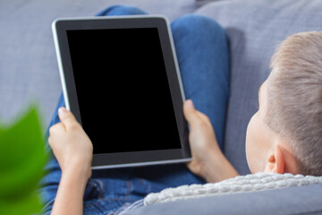 Kid using digital tablet computer and showing blank screen lying on couch at home