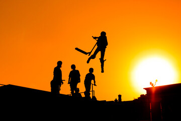 Unrecognizable teenage boy silhouette showing high jump tricks on scooter against orange sunsetwarm sky at skatepark. Sport, extreme, freestyle, outdoor activity concept