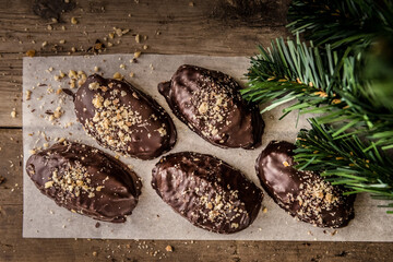 Chocolate covered Greek Melomakarona on wooden table next to christmas tree. Top view.