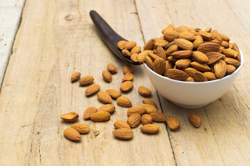 Almond nuts in white bowl with wooden spoon on wooden background,copy space.food vegetarian.