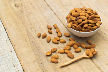 Almond nuts in white bowl with a wooden spoon on wooden background, copy space.vegetarian food