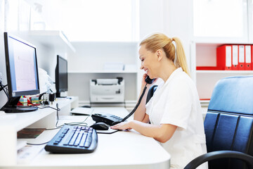 Smiling attractive blond female lab assistant in white sterile uniform sitting in laboratory and...