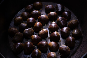 Close-up chestnuts in perforated pot on wooden background. raw chestnuts autumn fruits