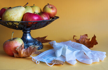 Vintage vase with apples, pears on a yellow background, autumn leaves, protective gloves, mask. Concept of fruit harvest during the coronavirus pandemic. Close - up, selective depth of field