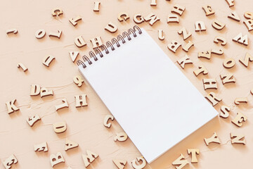 Notepad with an open blank page and wooden English letters on a light surface. Concept for alphabet, writing and journalism, storytelling, learning.