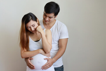 young caucasian husband embracing young pregnant asian belly wife with white background