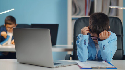 Fototapeta premium Tired and stressed little businessman working on laptop at office.
