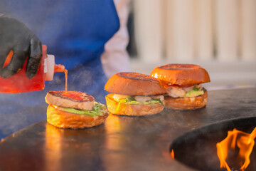 Chef preparing burgers with seafood, fish cutlet, shrimp, prawn on brazier with hot flame at summer local food market - close up view. Outdoor cooking, gastronomy, cookery, street food concept