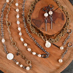 Trendy chokers, chains and earrings with pearls on a wooden stand. Fashion Jewelry. Top view