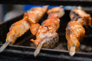 Process of cooking salmon skewers on grill over charcoal at summer local food market - close up. Outdoor cooking, barbecue, gastronomy, seafood, cookery, street food concept