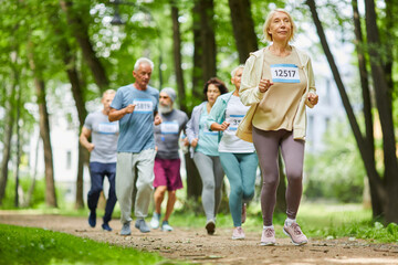 Group of modern active senior men and women spending day time together in park running marathon, wide shot