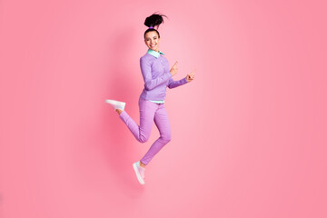 Fototapeta na wymiar Full length profile photo of sporty girl jump direct fingers empty space wear purple jumper pants sneakers isolated pink color background