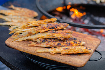 Crispy breaded european smelt fish on wooden cutting board at summer outdoor food market: close up. Seafood, barbecue, gastronomy, cookery, street food concept
