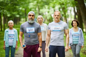 Medium long group portrait shot of active senior participants of marathon race in forest park looking at camera