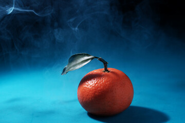 One fresh tangerine with leaves lies on a blue wooden table. Mysty photography with empty space for text