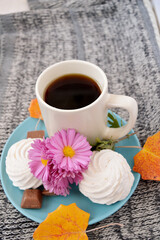 Ceramic cup with tea on a pale turquoise plate with pieces of milk chocolate, handmade marshmallows, autumn yellow-orange alder leaves and chrysanthemum flowers on a gray sweater background