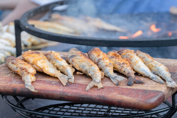 Crispy breaded european smelt fish on wooden cutting board at summer outdoor food market: close up. Seafood, barbecue, gastronomy, cookery, street food concept