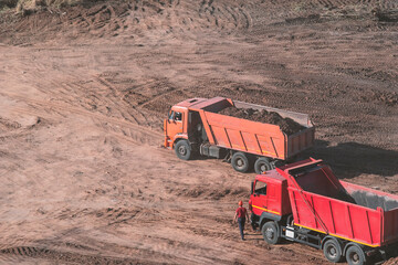 Two A red and orange dump truck stands on the sand View from above. Copy space for left and top text labeling