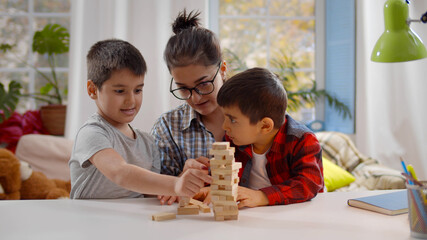 Happy young mother and two little children sitting at table and playing together