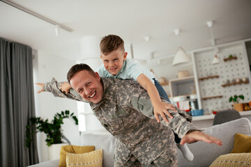 Soldier having fun with his son at home. Father and son playing in living room.