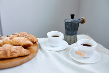 Two coffee cups and Italian coffee maker with croissant over table at home morning breakfast rituals concept, lifestyle food background..