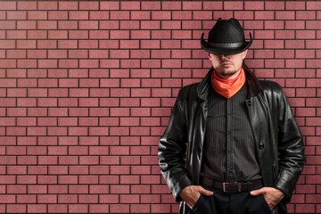 Man in a hat and a raincoat against the background of a red brick wall.