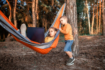 Cute kid using digital gadget for reading and learning in hammock, online education