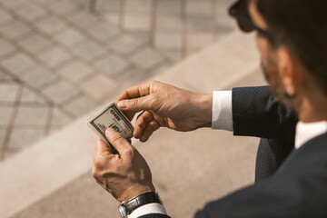 Businessman in black suit with bristles and glasses counting his fee in dollar terms while sitting...