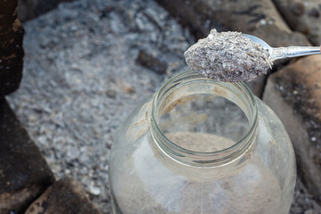 Spoon pours fresh wood ash into a glass storage jar