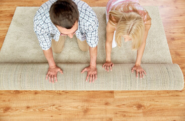 people, repair and renovation concept - happy couple unrolling carpet or rug on floor at home