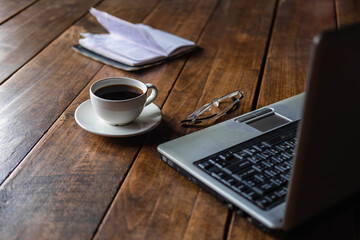 A coffee cup on the desk that has glasses and a notebook computer
