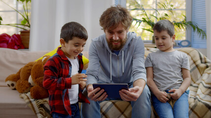 Young father and two sons using tablet computer spending time together sitting on couch